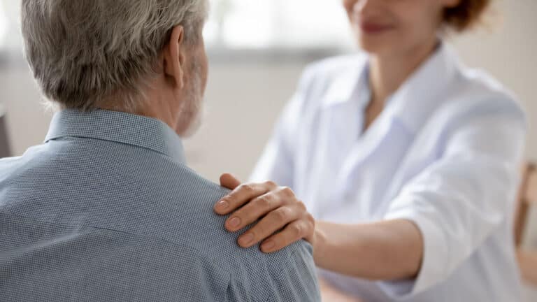 Woman putting hand on senior's shoulder for compassion