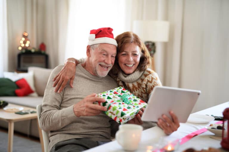 Happy older adult showing his Christmas present through a video call.