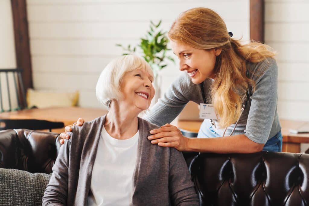 Female caregiver taking care of older woman indoors. 