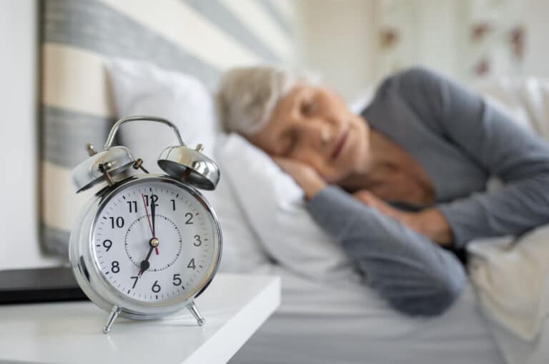 Older woman sleeping with an alarm clock in front of her